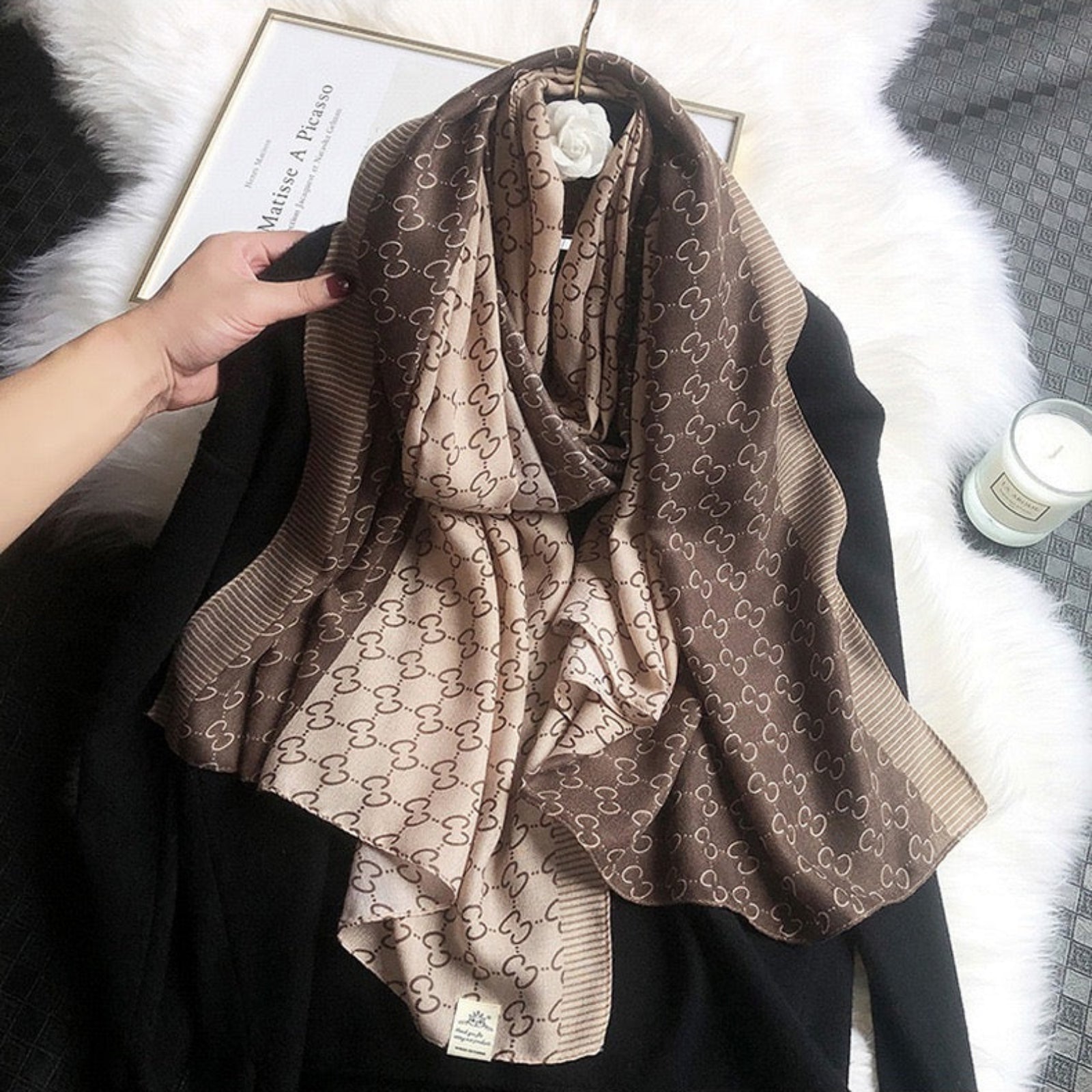 Brown patterned scarf draped over a black garment on a white surface.