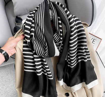 A striped Niket Opulent scarf in black and white, draped over a coat, with a focus on the intricate pattern.
