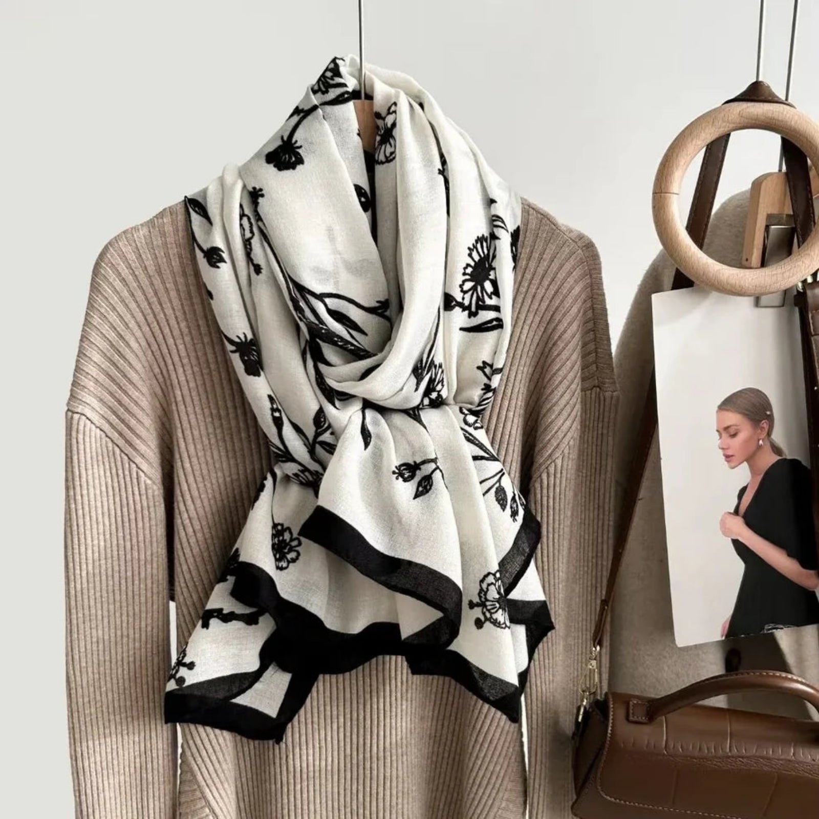 Beige sweater with a black and white floral patterned scarf, brown handbag, and magazine on a light gray background