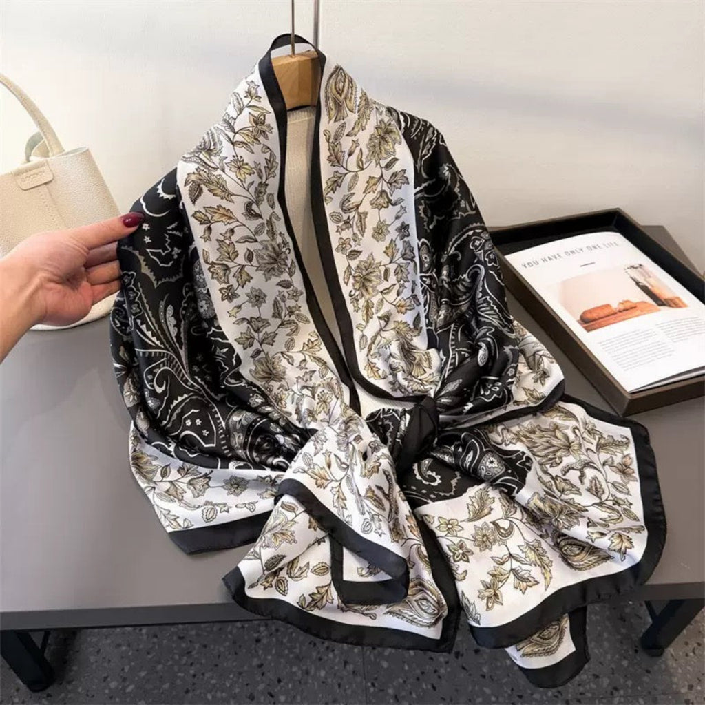 Black and white patterned scarf on a hanger with a hand holding it, placed on a table.