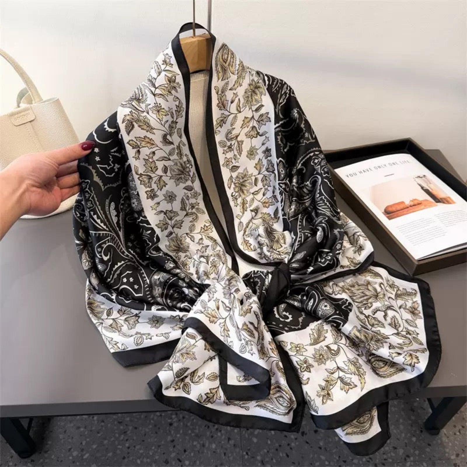 Black and white patterned scarf on a hanger with a hand holding it, placed on a table.