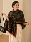 Elegant woman styling the Paisley Print Silk Scarf draped around her shoulders, featuring intricate teal and copper paisley motifs on a rich black base with satin striped borders.