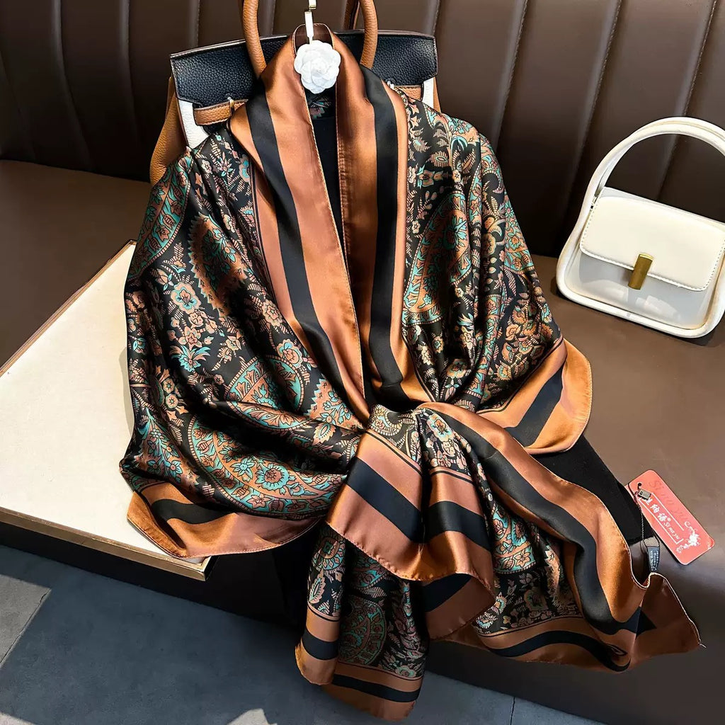 Flat lay view of the Paisley Print Silk Scarf highlighting its ornate paisley artwork, smooth silk-like finish, and contrasting copper and black satin border detailing.