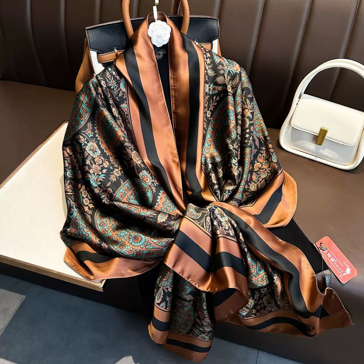Flat lay view of the Paisley Print Silk Scarf highlighting its ornate paisley artwork, smooth silk-like finish, and contrasting copper and black satin border detailing.
