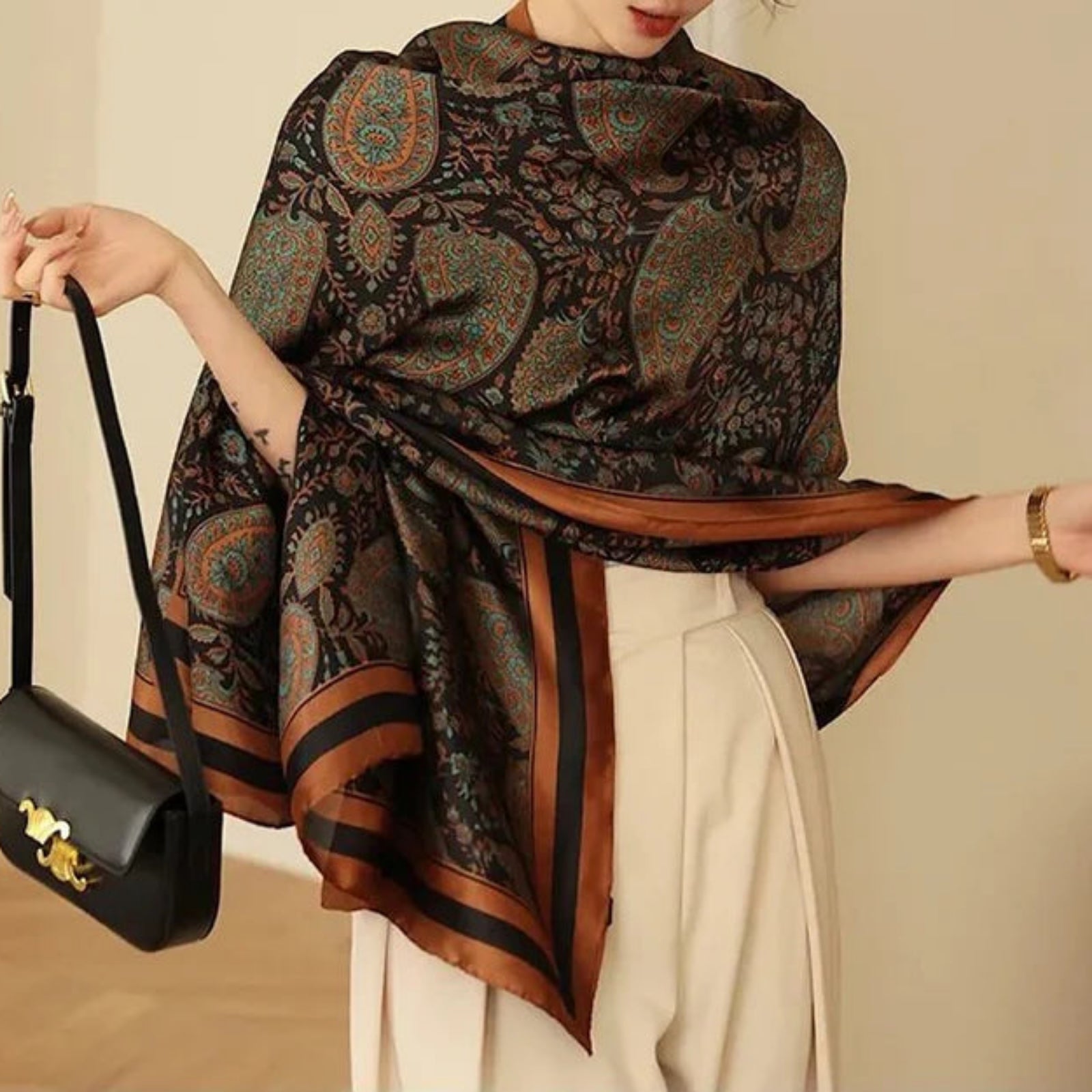 Person wearing a patterned scarf holding a black handbag against a neutral background