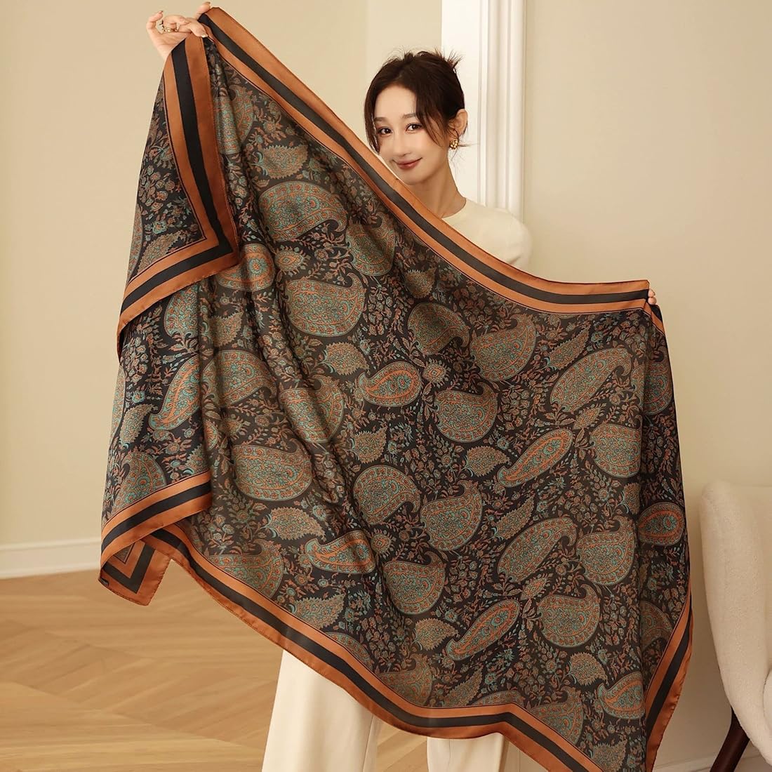 Woman holding a large patterned scarf in a room with a neutral background
