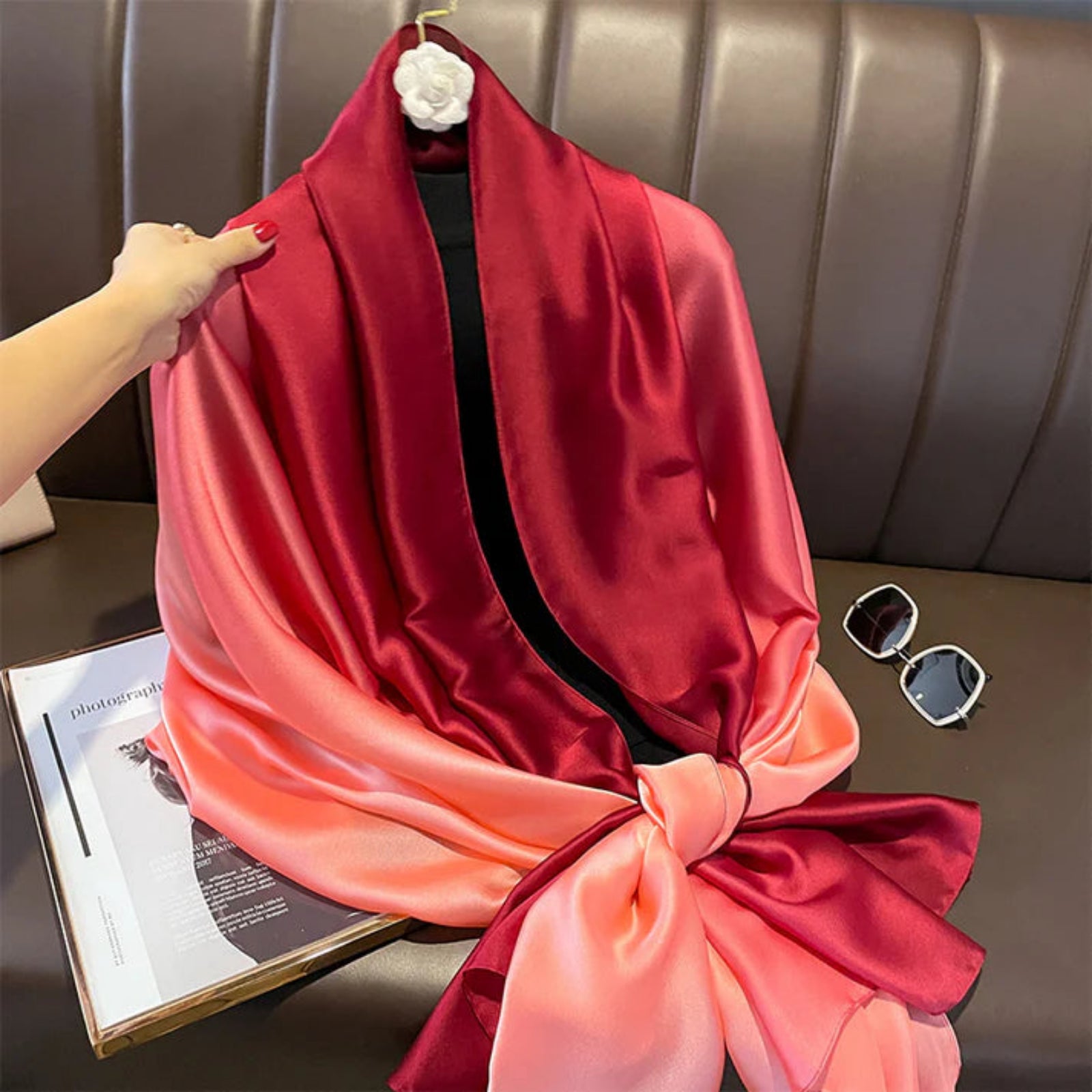 Red and pink gradient scarf on a hanger with sunglasses and magazine underneath.