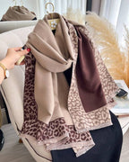 Beige and brown leopard print scarf draped over a chair with a blurred indoor background.