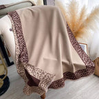 Beige blanket with leopard print border draped over a chair in a room with white curtains and pampas grass.