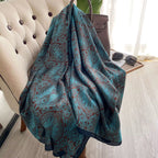 Teal patterned blanket draped over a chair with sunglasses on a table in the background.