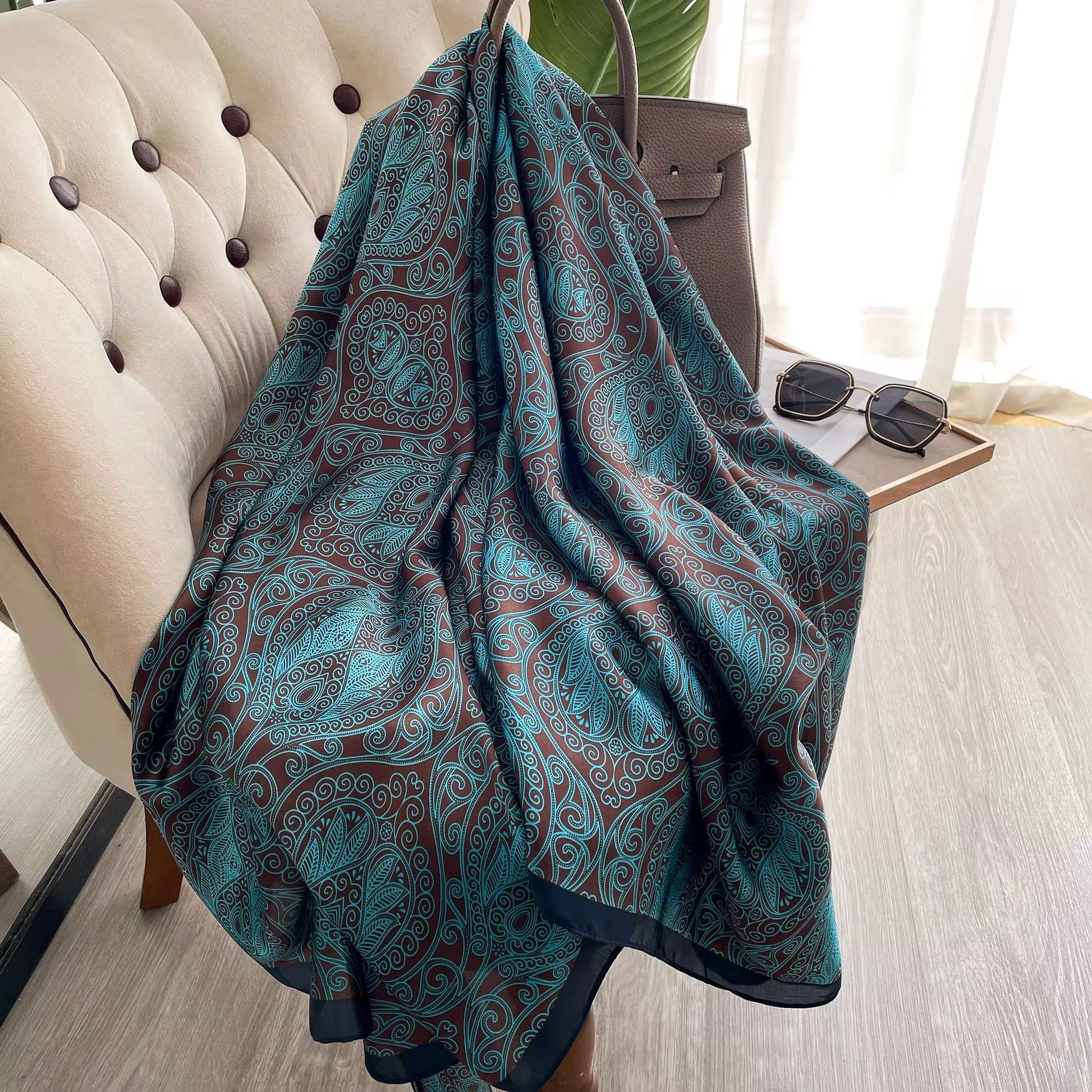 Teal patterned blanket draped over a chair with sunglasses on a table in the background.
