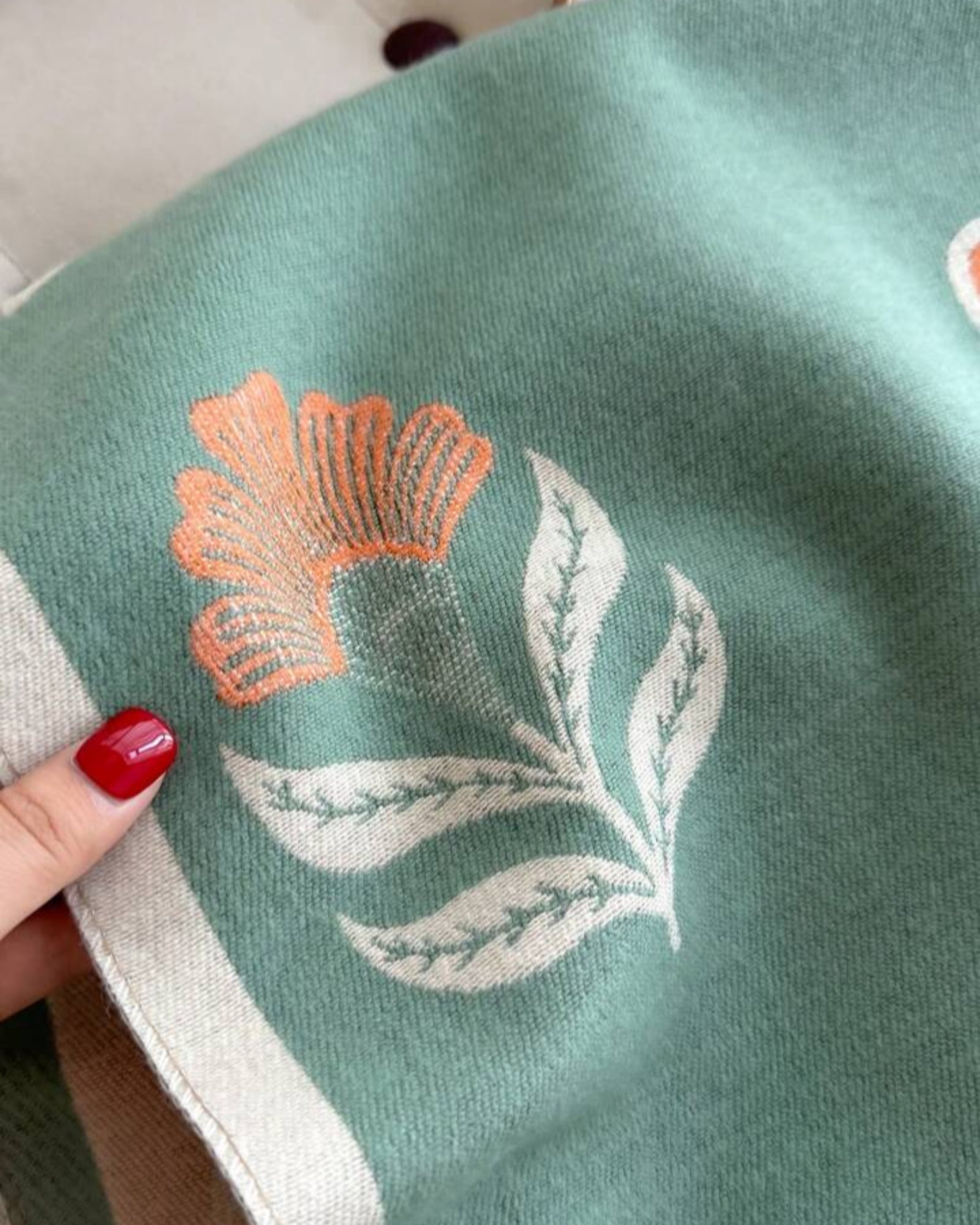 Embroidered flower and leaf design on a green fabric with a hand holding it.