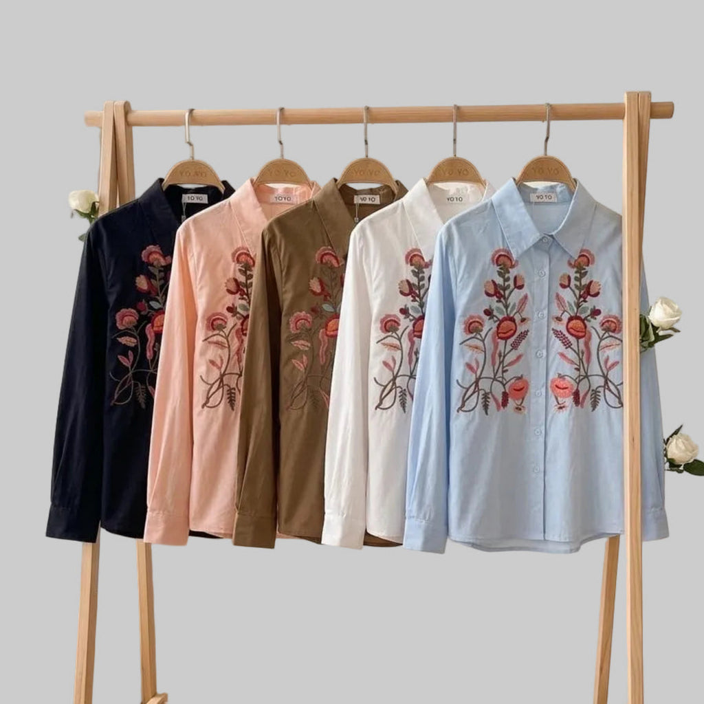 Five embroidered shirts on a wooden rack with a white wall background