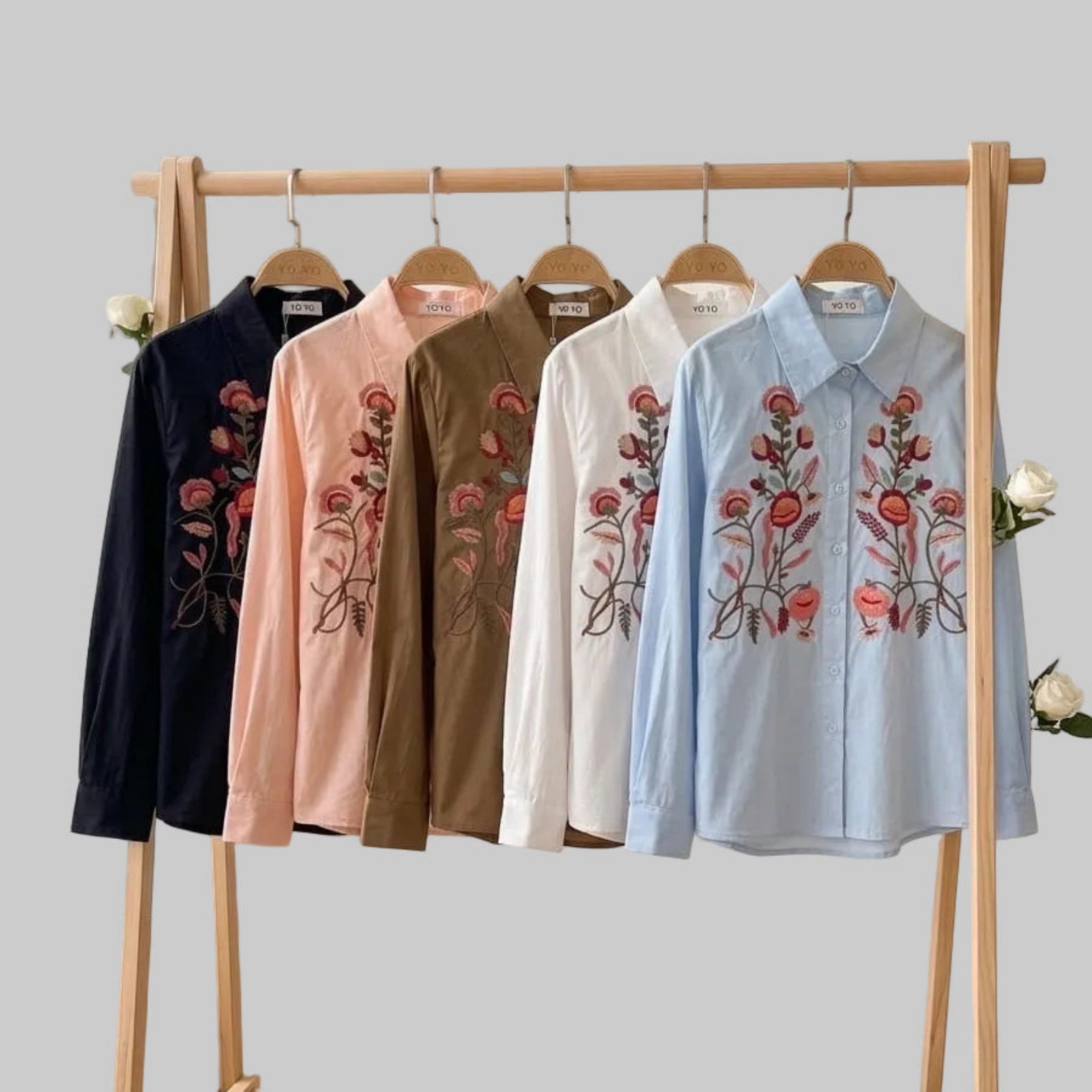 Five embroidered shirts on a wooden rack with a white wall background
