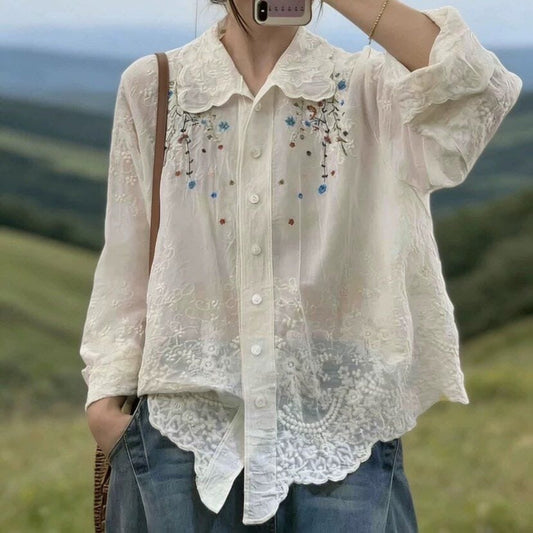 Person wearing a white embroidered blouse with a blurred natural background