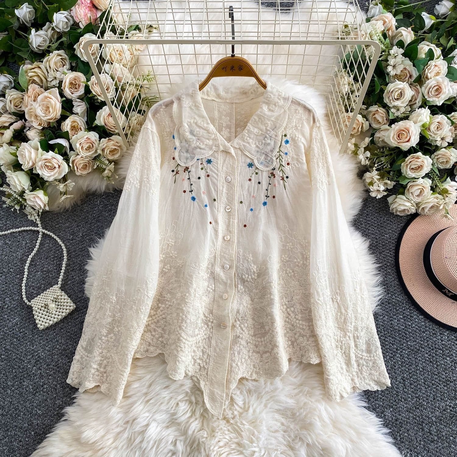 White lace blouse with floral embroidery on a hanger against a floral and textured background