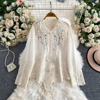 White lace blouse with floral embroidery on a hanger against a floral and textured background