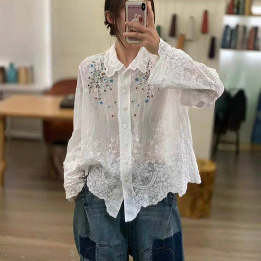 Person wearing a white lace blouse with embellishments in an indoor setting.