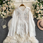 White embroidered blouse on a hanger with floral decorations and a hat in the background