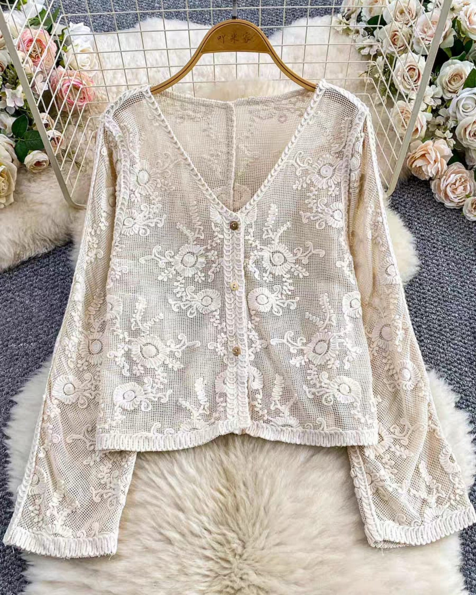 White lace cardigan on a hanger with floral decorations in the background