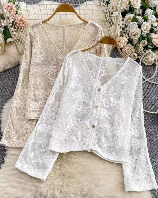 Two lace blouses on hangers with floral decorations in the background