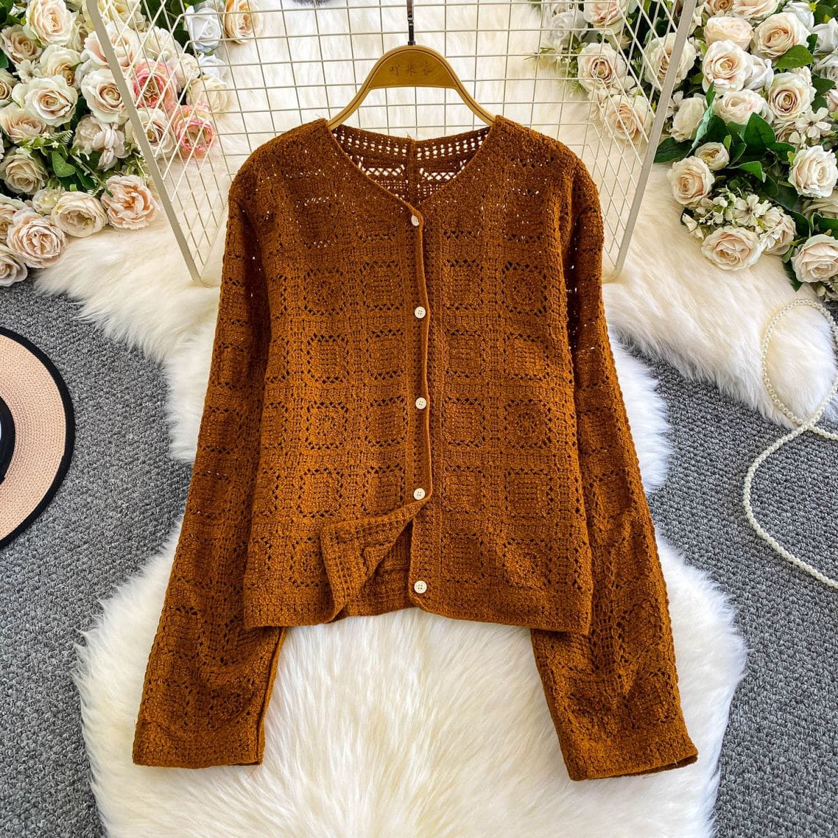 Brown knitted cardigan on a hanger with floral decorations in the background