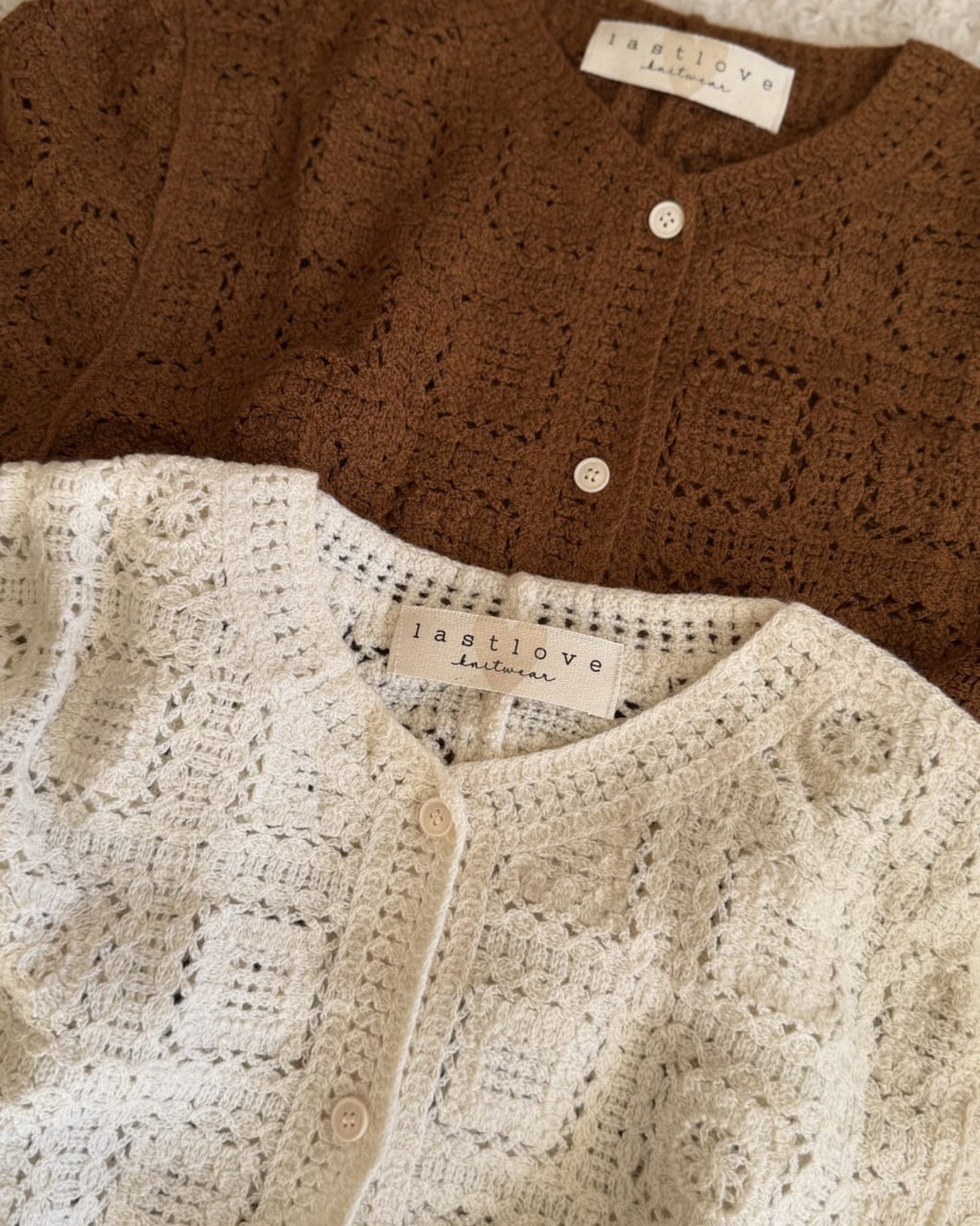 Two knitted cardigans, one brown and one beige, with 'lastlove' labels on a textured surface.