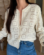 Person wearing a white crochet cardigan and blue jeans indoors.