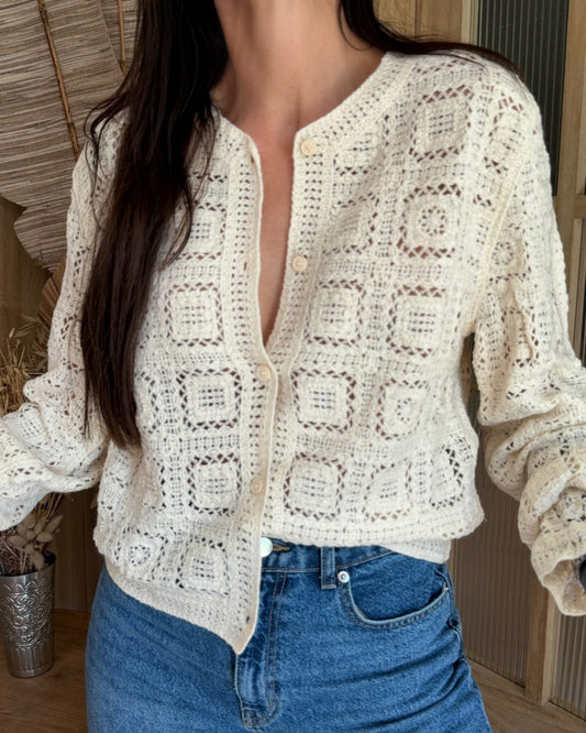 Person wearing a white crochet cardigan and blue jeans indoors.