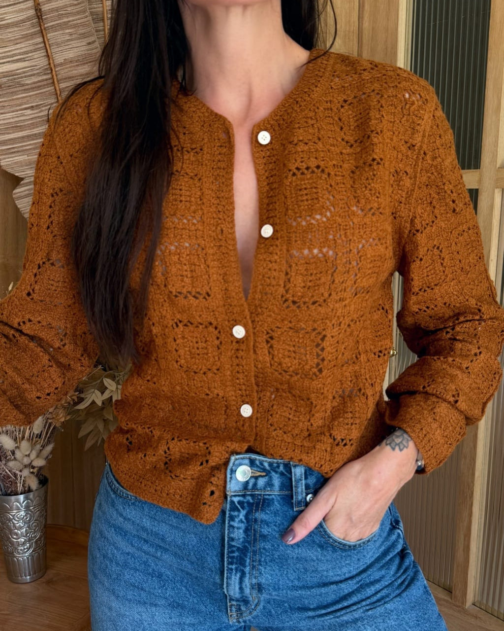 Person wearing a brown knitted cardigan and blue jeans indoors.