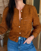 Person wearing a brown knitted cardigan and blue jeans indoors.