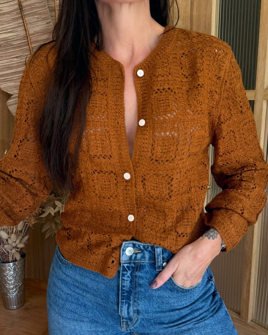 Person wearing a brown knitted cardigan and blue jeans indoors.