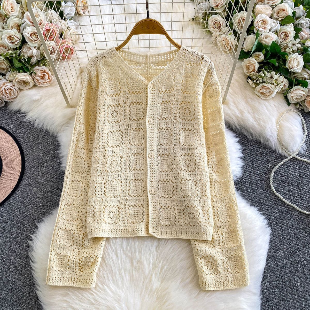 Beige crochet cardigan on a hanger with floral decorations in the background