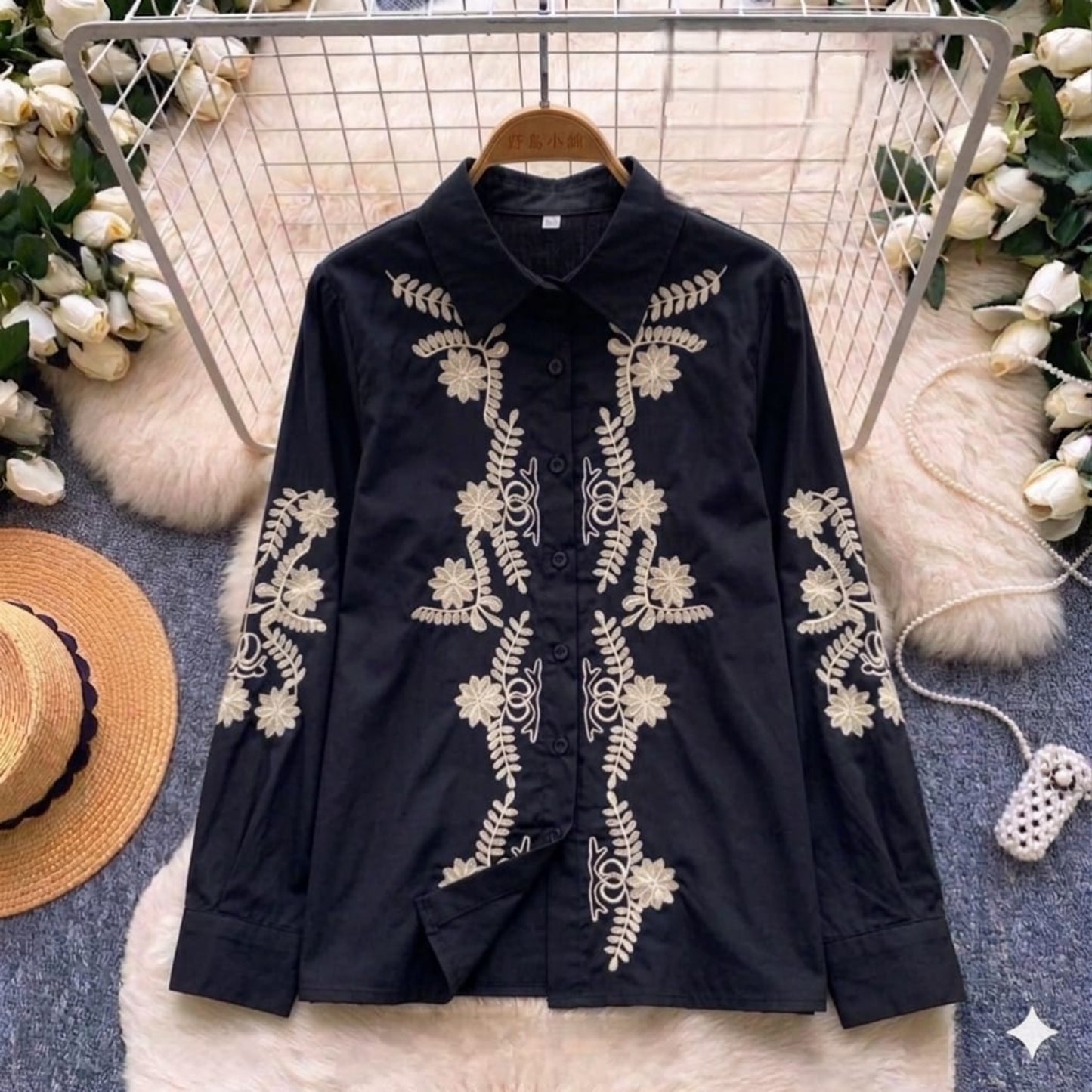 Black shirt with white floral embroidery on a hanger with decorative background