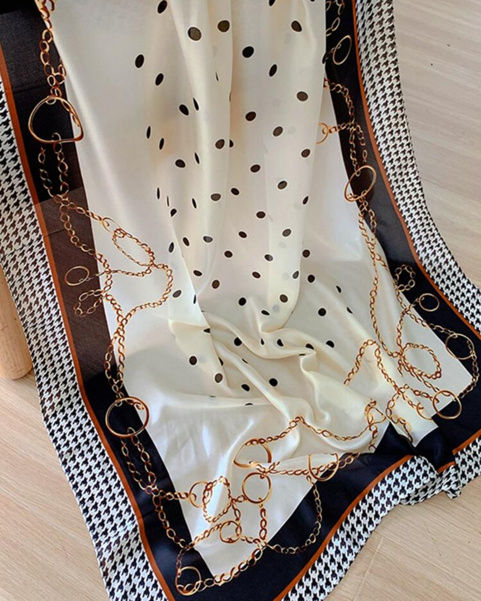 White polka dot scarf with gold chain details on a textured surface