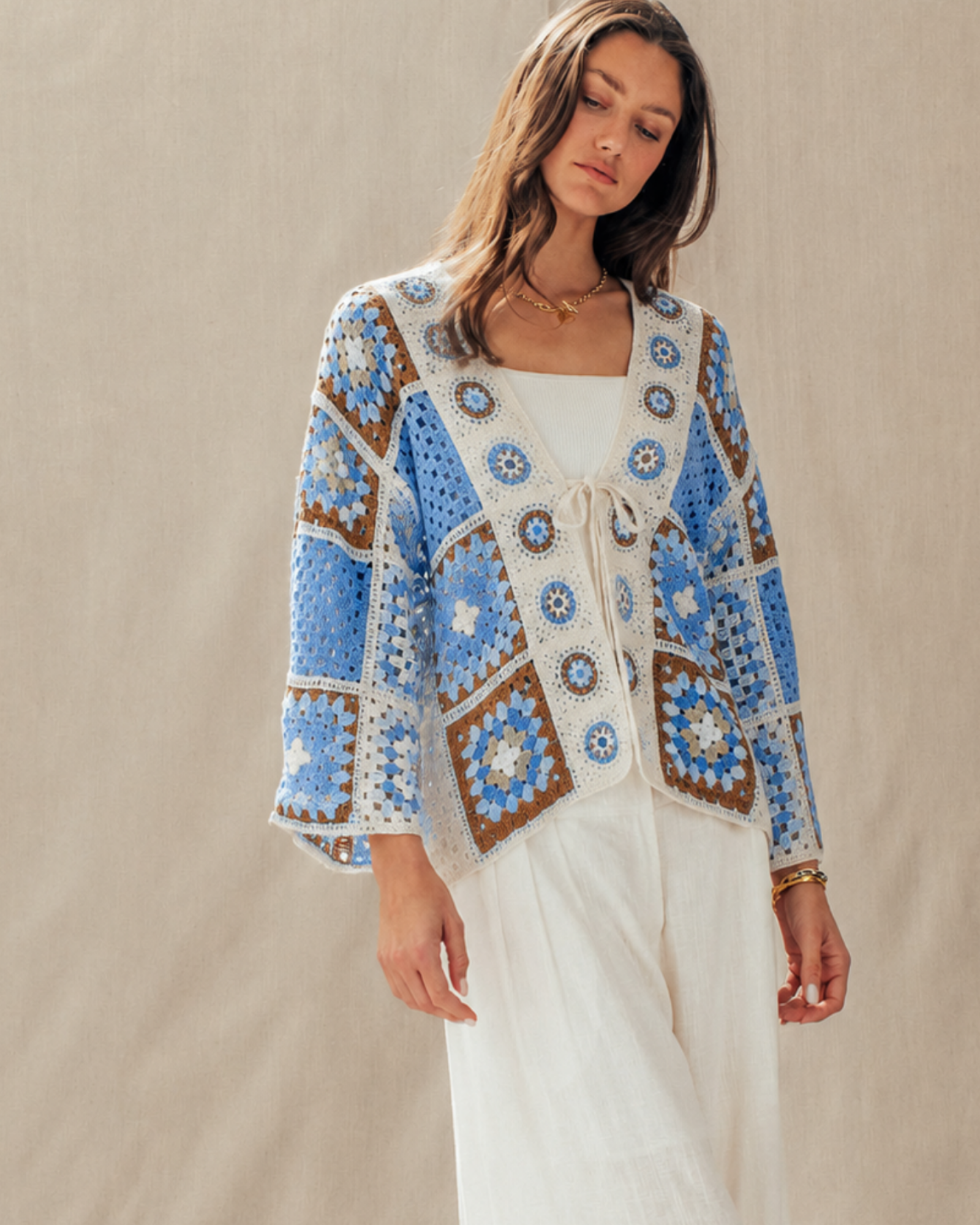 Woman wearing a blue and white patterned cardigan over a white dress on a beige background