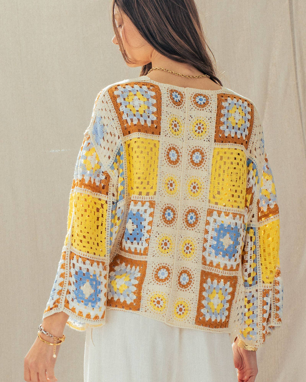 Person wearing a colorful crochet sweater with a neutral background