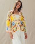 Woman wearing a colorful crochet cardigan and white pants against a beige background