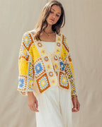 Woman wearing a colorful crochet cardigan and white pants against a beige background