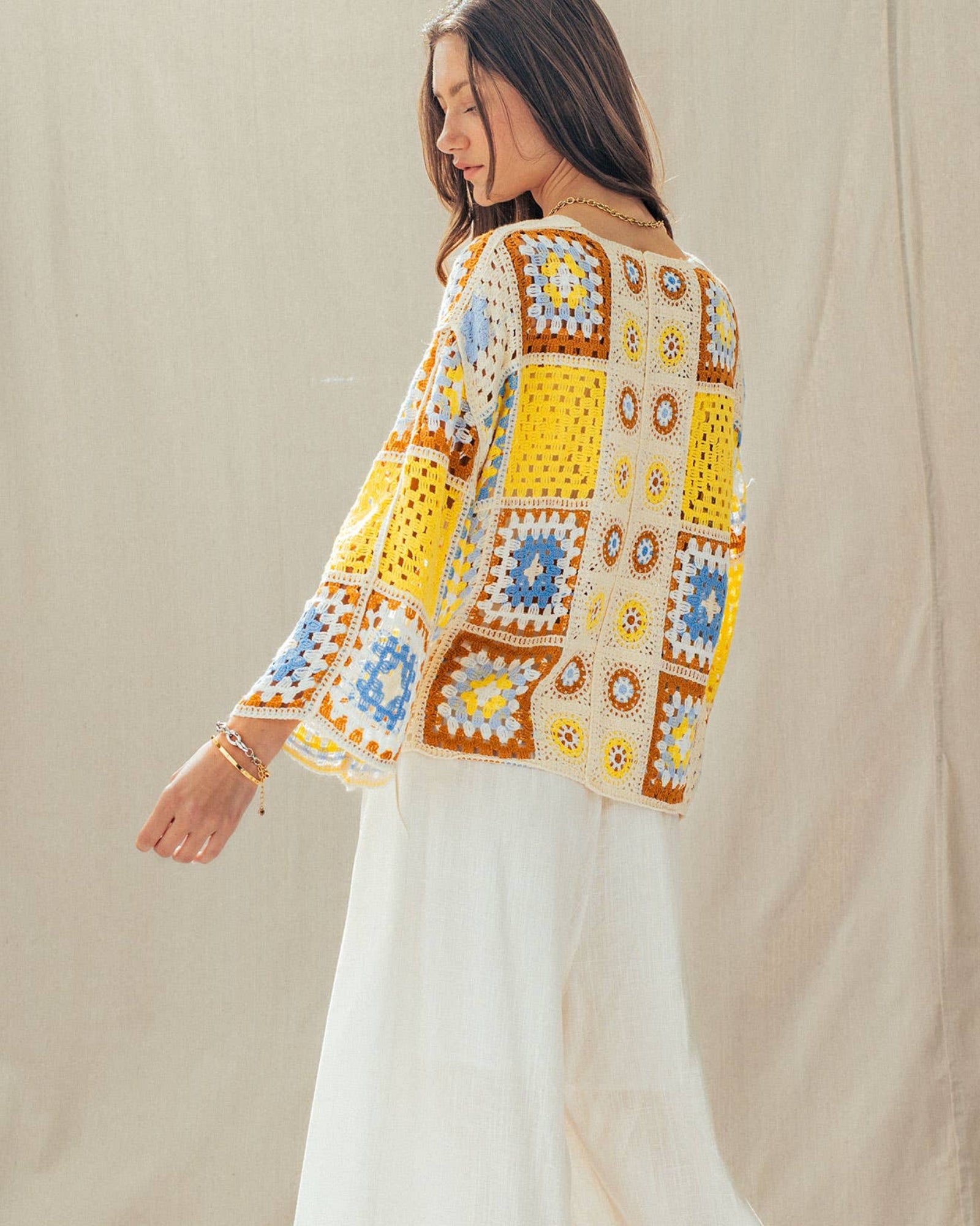 Woman wearing a colorful crochet top and white pants against a neutral background