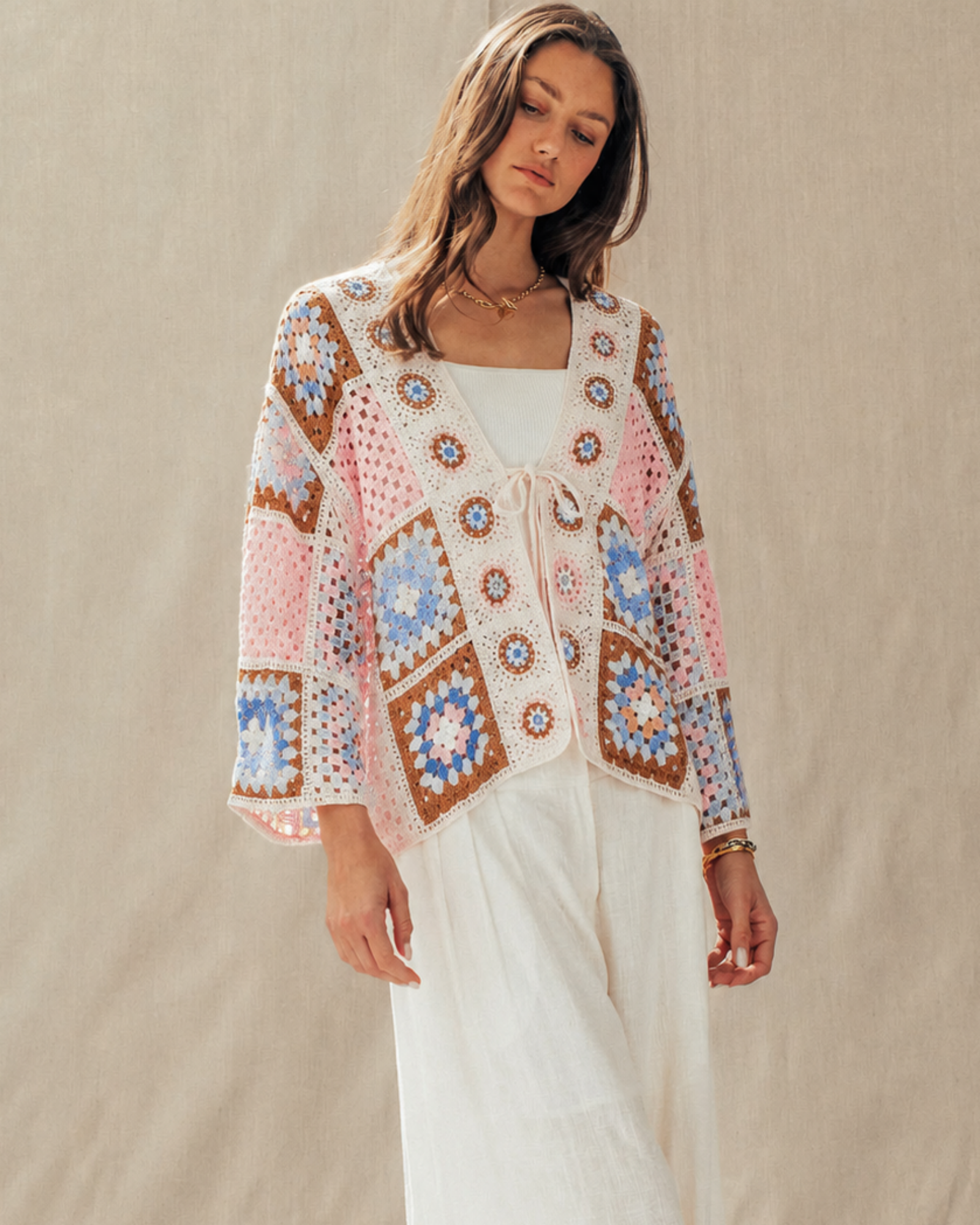 Woman wearing a colorful patterned cardigan over a white dress on a beige background