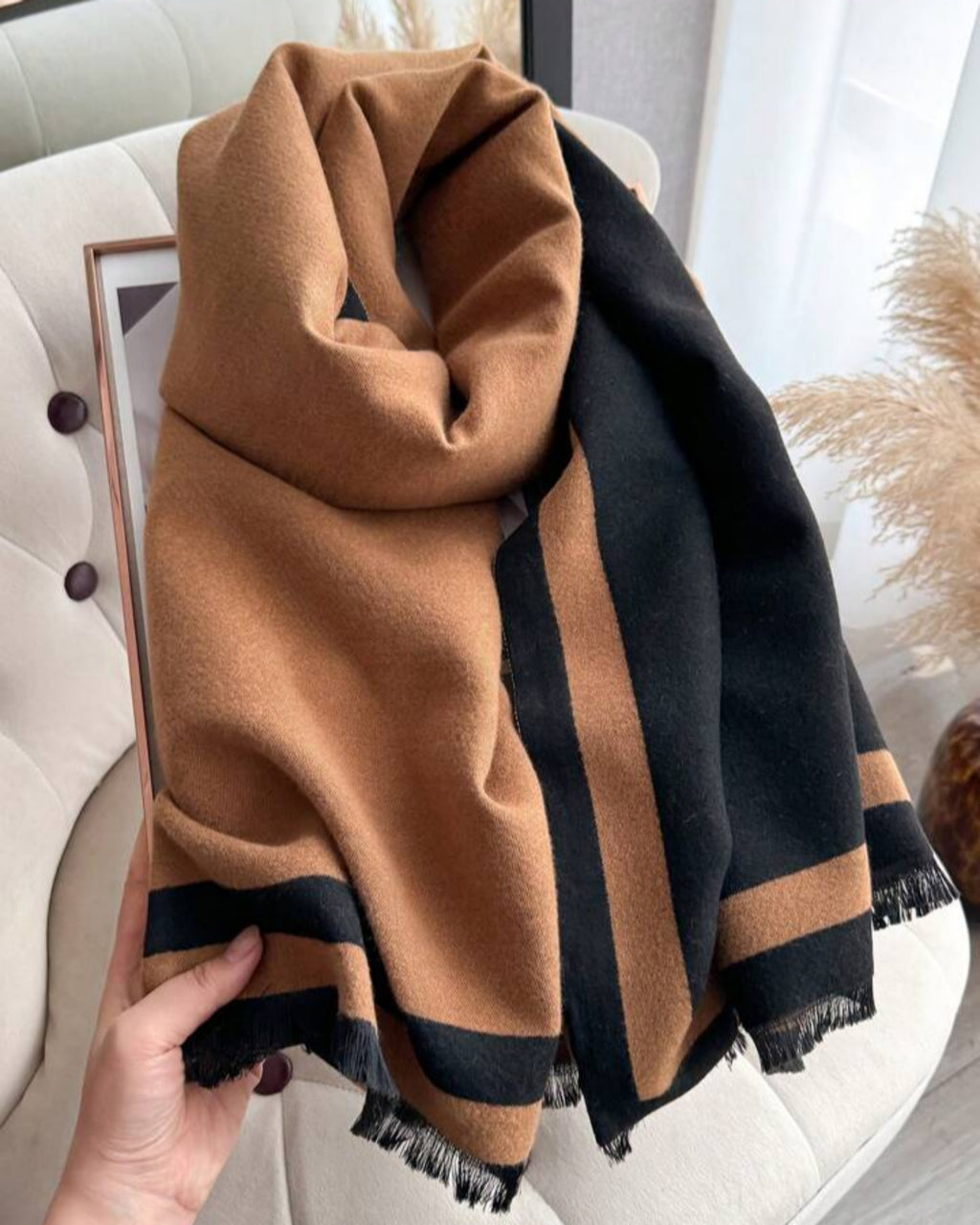 Brown and black striped scarf held by a hand on a light-colored surface.