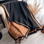 Black and brown blanket draped over a chair with a neutral background