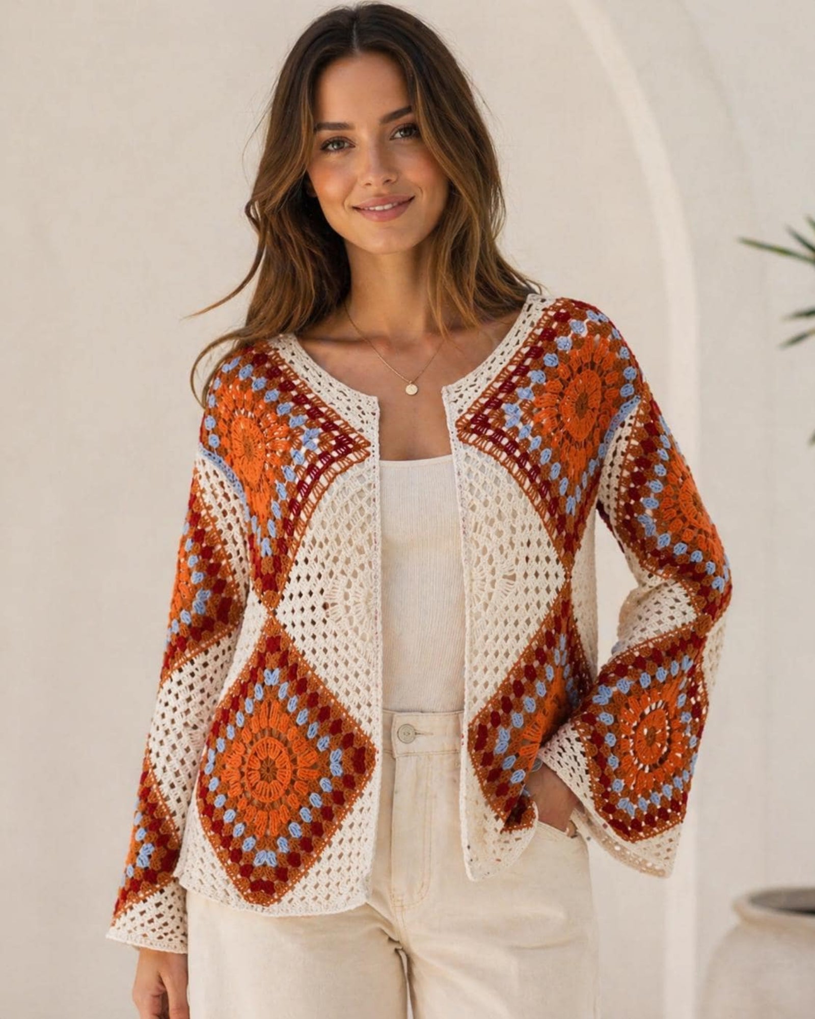 The Soleil Granny Square Crochet Jacket in Terracotta colourway — open-front boho crochet cardigan with mandala granny square panels in burnt orange, burgundy and sky blue on cream base, long bell sleeves, worn open over white cami and cream trousers, free size fits bust 42 inches