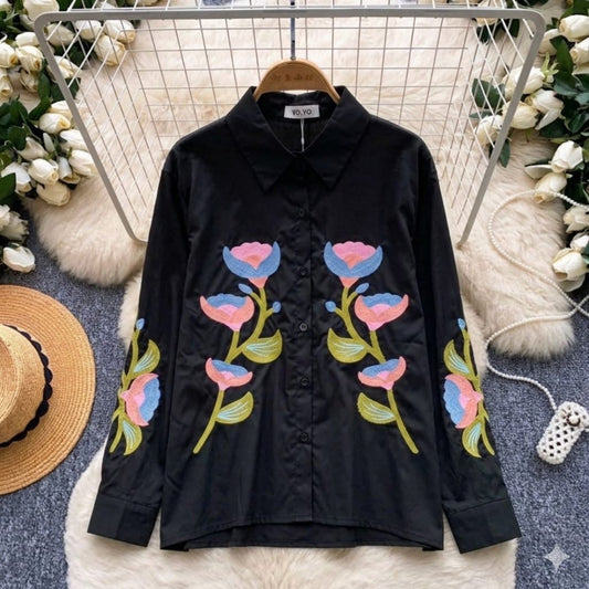 Black shirt with colorful floral embroidery on a hanger with decorative background