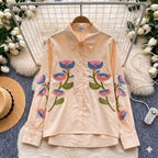 Pink shirt with floral embroidery on a hanger against a decorative background