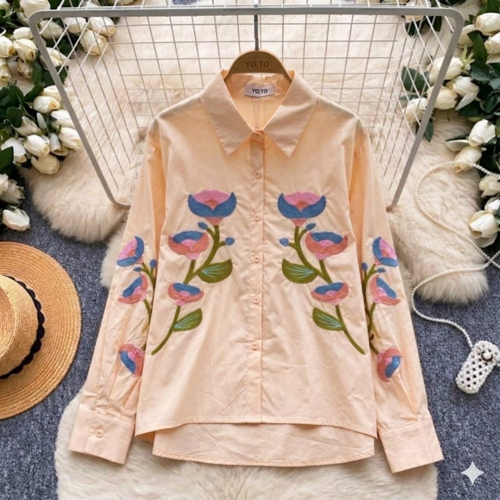 Pink shirt with floral embroidery on a hanger against a decorative background