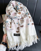 Floral patterned scarf with tassels held by a hand against a gray background