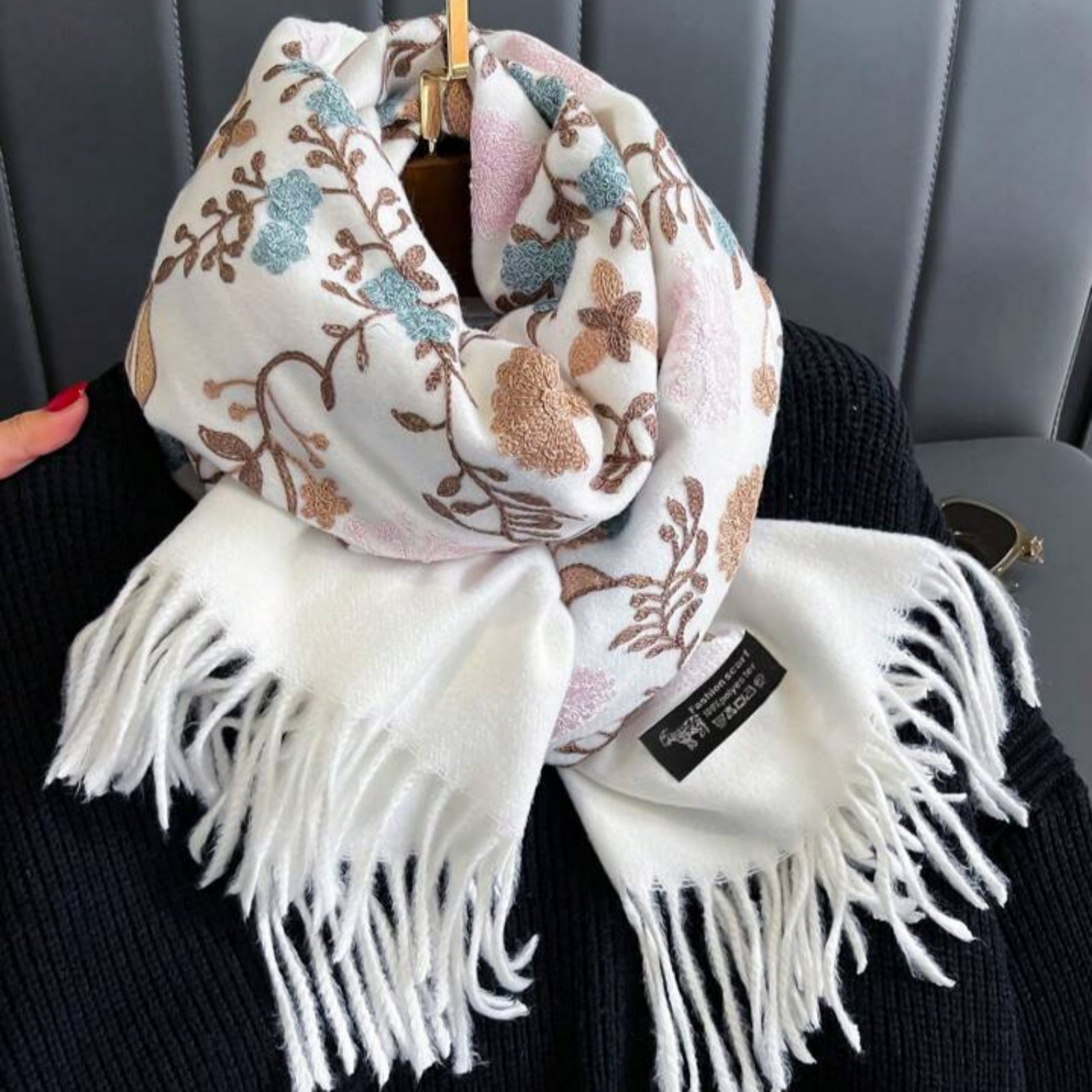 Floral patterned scarf with white fringe held by a person against a gray background