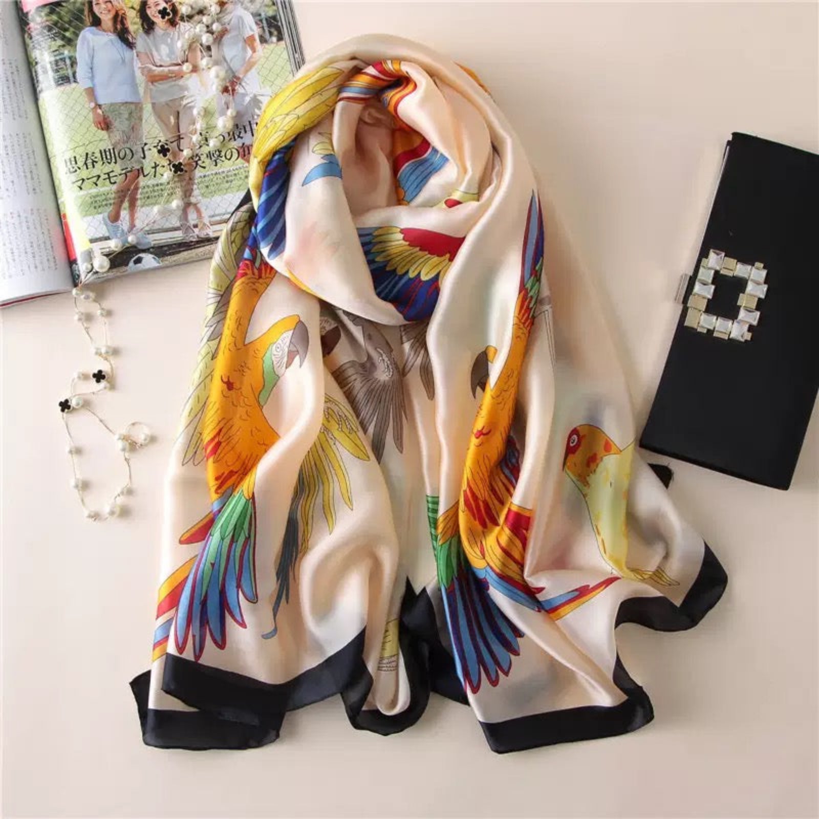 Colorful parrot scarf on a white surface with books and a necklace.